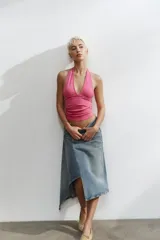 Falda midi de denim con diseño asimétrico en el bajo. Presenta tiro medio, trabillas para cinturón, cinco bolsillos clásicos y cierre frontal con cremallera y botón metálico.