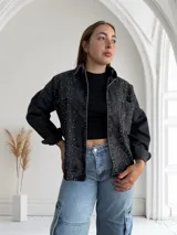 Campera de jean negra con tachas plateadas, corte recto, cuello camisero y cierre frontal con botones.