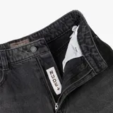 Pantalón de jean negro con corte baggy, de tiro medio y pierna ancha. Presenta un parche de cuero naranja en la cintura trasera y un bolsillo trasero con un parche bordado de la marca Nude Project. El ruedo tiene un acabado deshilachado.