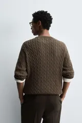 Jersey de punto color marrón oscuro, con cuello redondo y manga larga. Presenta un tejido con estructura de ochos y acabados en rib.