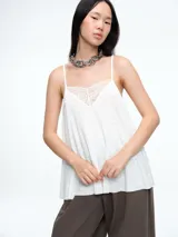 Top lencero de tirantes finos, color blanco, con escote en V decorado con encaje. Presenta una silueta holgada y liviana.