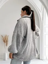 Camperón gris de tela tipo peluche con cierre frontal y bolsillos laterales.