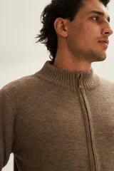 Campera tejida color marrón claro con cierre delantero, cuello alto y bolsillos delanteros. Tejida en 100% lana fina sin teñir.