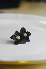 Par de caravanas con forma de flor, con centro dorado y pétalos en color negro, rojo y azul.