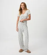 Pijama largo de dos piezas confeccionado en tejido peach touch, con estampado de cuadros y pequeños detalles florales. Incluye una blusa de manga corta con escote en V, frunce en el busto y bordes ondulados, y un pantalón de corte recto con cintura elástica y cordón ajustable.