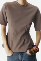 Remera de manga corta color marrón topo en punto interlock pesado, con cuello redondo y diseño entallado en la cintura con pinzas moldeadoras en el frente que generan una silueta peplum.