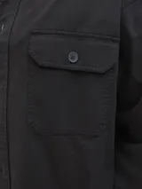 Sobrecamisa de manga larga confeccionada en sarga de algodón, con cuello camisero, cierre frontal de botones y un bolsillo en el pecho. Presenta un corte amplio y estructurado.