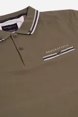 Remera polo azul marino de manga corta, con cuello y puños a rayas blancas y verde militar. Presenta un bolsillo en el pecho con detalle de franja a rayas y el logo de la marca "Brooksfield" bordado en dorado.