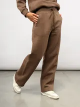 Pantalón de corte recto confeccionado en felpa, con cintura elástica ajustable mediante cordón y bolsillos laterales. Presenta un diseño minimalista con el logo de la marca sutilmente bordado en la parte frontal.