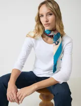 Pashmina cuadrada de satén con estampado multicolor en tonos turquesa, rojo y crema. Presenta un diseño artístico con motivos geométricos y figurativos.