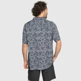 Camisa de manga corta confeccionada en viscosa, con cuello tipo solapa y cierre frontal de botones. Presenta un estampado tropical en tonos grises y negros, con un diseño ligero y fluido.
