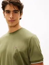 Remera de manga corta Tommy Hilfiger de corte slim en color verde militar, con cuello redondo clásico y detalle de doble raya blanca en los puños. Presenta el icónico logo de la marca bordado en el pecho.