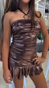 Vestido corto strapless de tela metalizada con acabado brillante. Presenta un diseño ajustado con frunces laterales y un ruedo con volado.