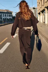 Chaqueta corta de color marrón oscuro, con cuello de solapa, manga larga con trabillas en los puños, bolsillos delanteros con solapa y cierre frontal con botones.