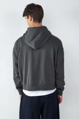 Buzo con capucha de corte holgado en color gris oscuro, con bolsillo tipo canguro frontal, cordones ajustables y puños acanalados.