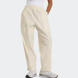 Pantalón de sarga color beige, con cintura elástica ajustable con cordón, bolsillos laterales de doble entrada, dobladillo con botón a presión y costuras inspiradas en la ropa utilitaria.