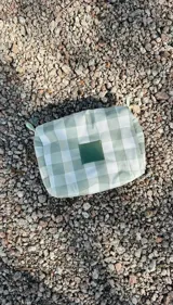 Necessaire rectangular de tela estampada a cuadros verdes y blancos, con cierre superior y etiqueta verde con logo.