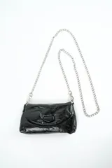 Cartera bandolera negra de charol con solapa frontal, cierre de broche imantado y correa larga de cadena metálica plateada.
