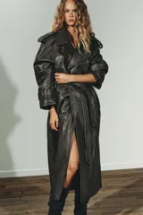 Trench coat de Zara con efecto piel texturizada en color gris oscuro. Presenta cuello con solapas, cierre frontal cruzado con botones, cinturón lazada del mismo material, mangas largas con trabillas y abertura en la espalda.