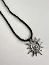 Collar con dije de sol en acero quirúrgico y cordón tipo tiento negro trenzado.