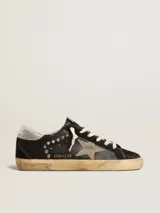 Zapatillas Golden Goose modelo Super-Star, confeccionadas en cuero negro con detalles en gamuza, estrella lateral gris y tachas metálicas plateadas. Cuentan con suela de goma con acabado envejecido y cordones de algodón crudo.