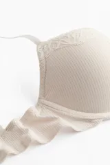 Soutien push-up color beige de punto acanalado, con copas acolchadas, aros, breteles ajustables y cierre de corchetes en la espalda. Presenta detalles de encaje en el borde superior de las copas y un pequeño lazo en el centro.