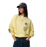 Buzo Rip Curl de fleece, modelo Sg Heritage Oversized, color amarillo, con cuello redondo y diseño holgado. Presenta un pequeño estampado circular en el pecho y letras estampadas en la manga.