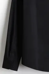 Camisa de vestir negra con cuello italiano, cierre frontal de botones y mangas largas con puños ajustables. Presenta un corte entallado y bajo redondeado.