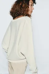 Jersey de punto color blanco crema, con escote en pico, manga larga y sisa ancha terminada en puño.