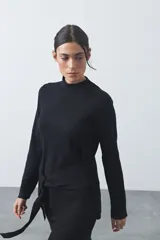 Polera de tejido de punto color negro, con cuello alto, manga larga y lazo ajustable en la cintura que aporta estructura a la silueta.