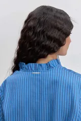 Camisa de manga larga con diseño a rayas verticales en tonos azules. Presenta un cuello mao con detalle de volados a lo largo de la abertura frontal y mangas abullonadas con puños elásticos.