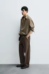 Camisa de manga larga color marrón verdoso, con cuello solapa y cierre frontal de botonadura. Presenta un tejido con textura rústica y un calce relajado.