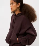 Hoodie de color marrón oscuro con diseño voluminoso tipo globo, capucha con cordón de ajuste, mangas largas abullonadas con pliegues y bolsillo canguro frontal.
