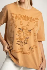 Remera color arena con estampa frontal de flores y texto "Les Tourness Bisou". Corte oversize.