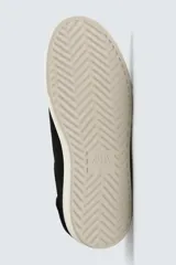 Zapatilla de piel color negro con acabado serraje, cordonera oculta y suela plana a contraste en color crema.