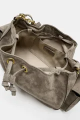 Mini bolso bandolera de piel color gris topo, con diseño fruncido, cierre mediante cordón ajustable y stopper, bolsillos exteriores laterales con solapa y botón imantado, y correa ajustable.
