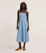 Vestido midi de denim color celeste, confeccionado en mezcla de algodón y lino. Presenta escote recto, breteles finos ajustables con lazos y falda con pliegues.