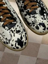 Zapatillas bajas con estampado animal print de vaca en blanco y negro, con cordones marrones y suela color caramelo.