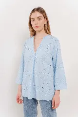 Camisa blanca de diseño suelto con cuello en V y mangas 3/4. Presenta detalles calados y bordados en un patrón geométrico.