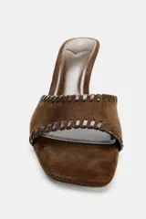 Sandalia tipo mule de gamuza color marrón, con tira delantera decorada con pespuntes en contraste, tacón fino y punta cuadrada.