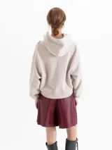 Buzo con cierre frontal y capucha, color beige, con estampado floral y de cadenas en el frente. La capucha cuenta con forro de corderito al tono, mangas largas con puños elásticos y ajuste holgado.