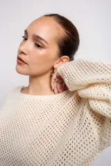 Buzo color crudo de tejido calado con transparencia, de corte holgado y mangas largas.