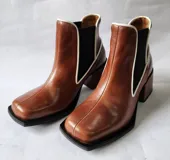 Bota tipo chelsea de cuero color óxido, con elástico lateral negro y ribetes en color crema. Presenta un taco cuadrado robusto y punta cuadrada.