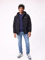 Campera impermeable Rusty con capucha, confeccionada en nylon. Presenta cierre frontal con botones a presión, bolsillos delanteros con solapa y puños elásticos.