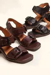 Sandalias de cuero negro con taco bloque de madera tallada, tiras con hebillas grandes y punta cuadrada.