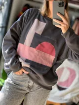 Buzo gris cemento de calce relajado, confeccionado en friza de verano, con diseño abstracto aplicado a mano mediante la técnica de patchwork en tonos rosados, bordó y beige.