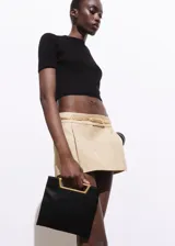 Bolso de mano tipo sobre con diseño cuadrado, confeccionado en poliéster negro. Cuenta con un asa metálica rígida en tono dorado y una cadena larga extraíble.