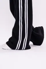 Pantalón deportivo tipo jogger de corte relajado, color negro con franjas laterales blancas y cintura elástica fruncida.