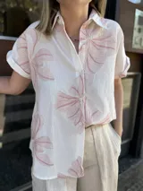 Camisa blanca de manga corta con cuello clásico y cierre frontal de botones, destacada por grandes bordados florales en tonos rosados.