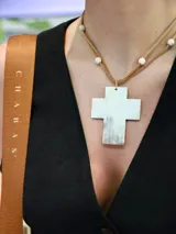 Collar con dije de cruz de guampa blanca, engarzado con hilo dorado. El collar es de cuero marrón con cuentas de piedra blanca.